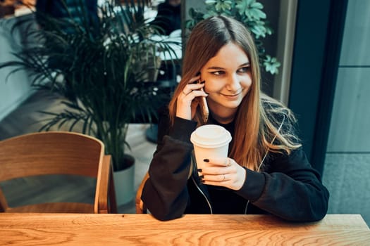 Young woman talking on the phone at cafe, having a pleasant phone call, answering call, chatting by mobile phone with friend while sitting in a cafe and drinking coffee. Girl relaxing in cafe
