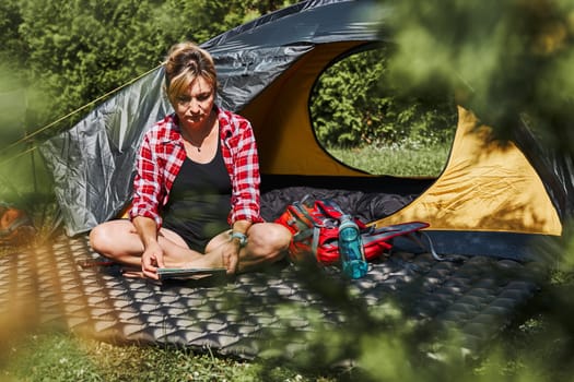 Woman planning next trip while sitting with map in tent. Woman relaxing in tent at camping during summer vacation. Actively spending vacations outdoors close to nature. Concept of camp life