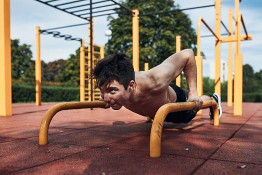 Young shirtless man bodybuilder doing push-ups on a parallel bars during his workout in a modern calisthenics street workout park
