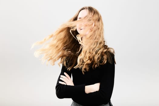 Portrait of pretty cheerful young woman waving tossing her hair holding arms crossed standing over a grey plain background