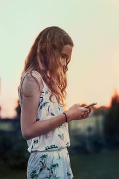 Young woman using mobile phone smartphone standing in a backyard. Candid people, real moments, authentic situations