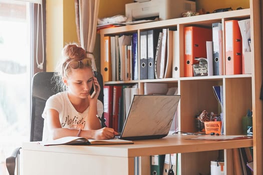 Young woman working at home, using portable computer, sitting at desk in home office. Candid people, real moments, authentic situations