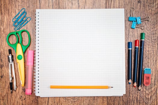 School accessories, pencil, pen, scissors, blank sheet of paper on a wooden desk. View from above