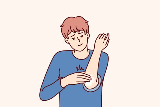 Man smears elbow with healing ointment after bruise or skin problems and acne. Young guy uses analgesic dermatological ointment to treat elbow joint and take care of skin in need of moisture
