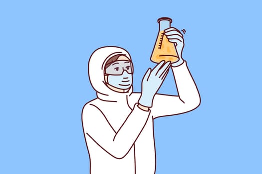Chemist laboratory assistant holds test tube with reagent examining hazardous substance, dressed in chemical protection clothing. Female chemist examines contents of flask after synthesis