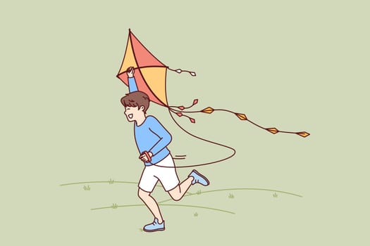 Little boy with kite runs through meadow enjoying summer walk with favorite toy. Happy kid laughing while flying kite for concept of carefree childhood and teen outdoor activity
