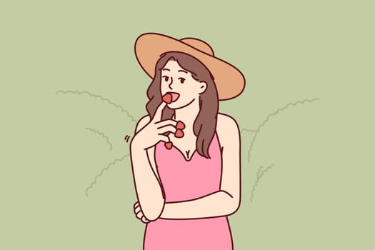 Woman eats appetizing strawberries enjoying taste of fresh berries found on farm or plantation. Girl in hat who owns farm tries organic strawberries grown without use of pesticides