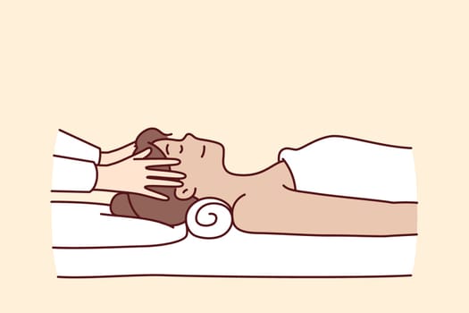 Woman in massage parlor lies on couch near hands of spa specialist doing facial rejuvenation procedure. Massage of head for getting rid of migraine and rejuvenating effect in cosmetology clinic