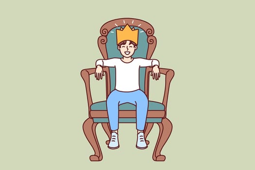Little boy sits on throne with crown on head dreaming of growing up to be prince or king. Teenager boy in golden crown made of paper laughs with eyes closed and imagining monarchy.
