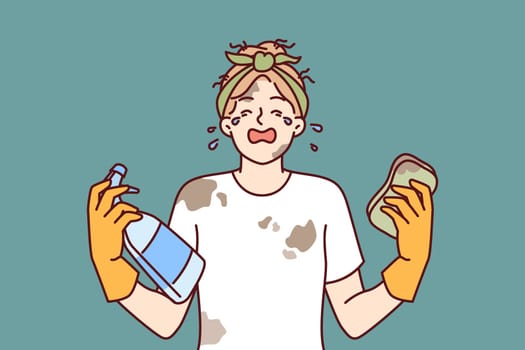 Woman housewife in dirty clothes is crying because of large amount housework and lack of rest. Girl housewife with tears in eyes holds sponge and spray bottle for cleaning in apartment