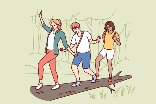 Group of friends participate in hike balancing on log thrown across river instead of bridge. Guy and two girls enjoy outdoor activities and hike in nature reserve with impenetrable terrain