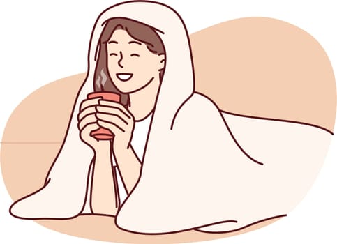 Girl with cup of hot coffee lies wrapped in blanket and smiles enjoying winter morning. Woman drinking hot drink with blanket to keep warm after walking on cold street for autumn mood concept
