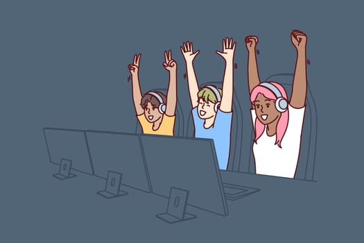 Team of teenagers esports or gamers have won multiplayer video game and are raising hands in triumph. Team of gamers are sitting at table with computers participating in cyber MMORPG tournament