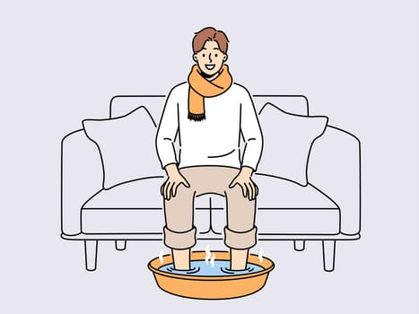 Smiling man in scarf sit on sofa at home soak feet in hot water. Happy male suffer from cold or flu do procedures for fast recovery. Healthcare. Vector illustration.