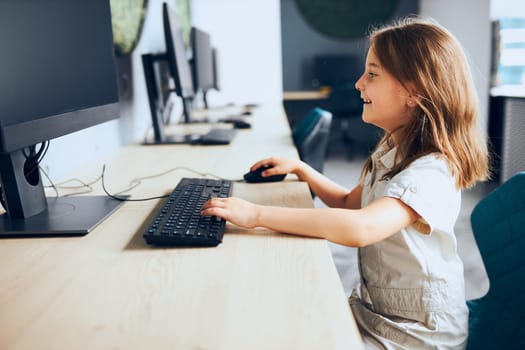Fascinating computer class. Child learning to use technology in classroom at primary school. Schoolgirl using computer on elementary computer science class. Smart little girl learning programming and coding at school. Engaged child solving riddles on personal computer. Back to school