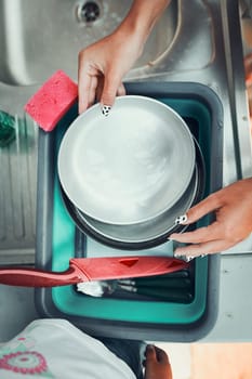 Teenager girl washing up the dishes pots and plates with help her younger sister in the outdoor kitchen during vacations on camping. Camp life. Sisters spending time and working together