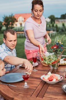 Family having a meal from grill during summer picnic outdoor dinner in a home garden. Close up of people sitting at a table with food and dishes