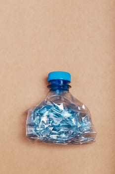 Squashed empty plastic bottle over cardboard background. Collecting plastic waste to recycling. Concept of plastic pollution and too many plastic waste. Copy space for text