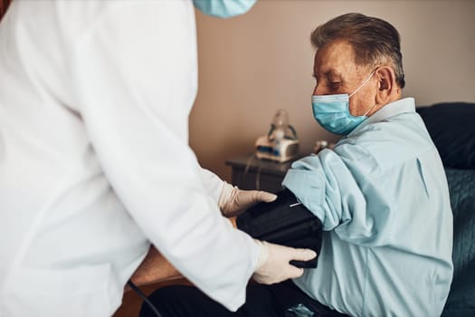 Doctor carying out blood pressure test and heart rate of senior man. Checking health condition elder patient suffering from arterial hypertension