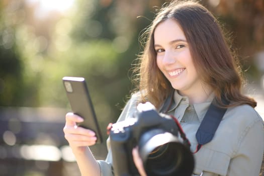 Happy photographer pairing cell phone with dslr professional camera looking at you