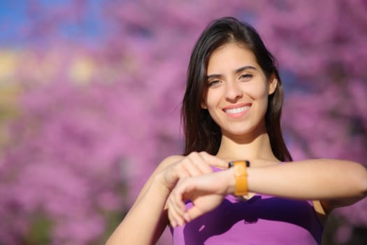 Front view portrait of a happy woman looking at camera using smartwatch