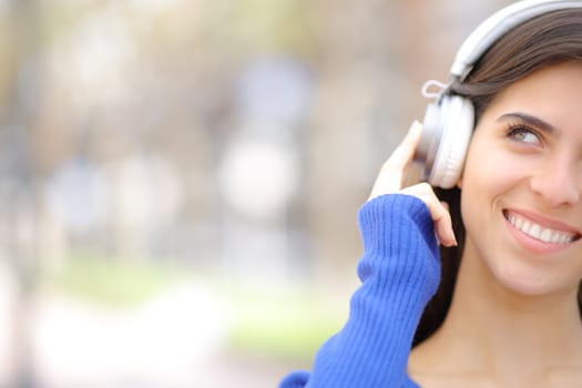 Front view portrait of a happy woman with headphone looks at side with copy space