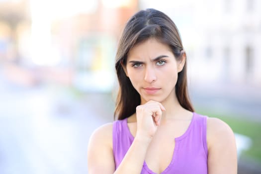 Front view portrait of a suspicious woman looking at camera standing in the street