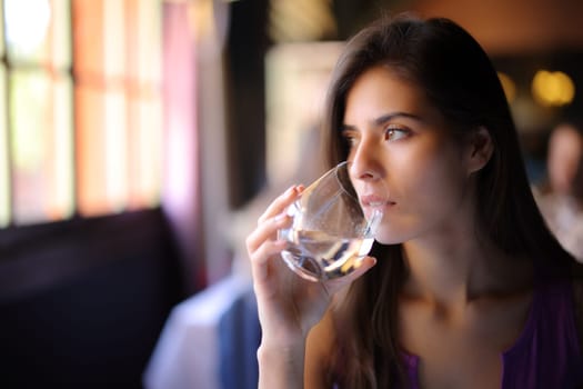 Serious woman drinking water sitting in a restaurant looking at side