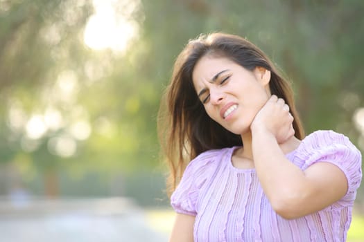 Stressed woman suffering neck ache alone in a park