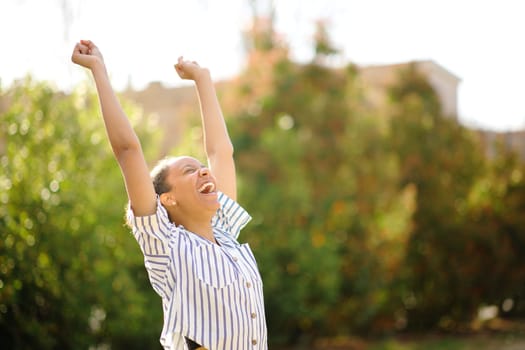 Excited black woman raising arms and screaming in a park