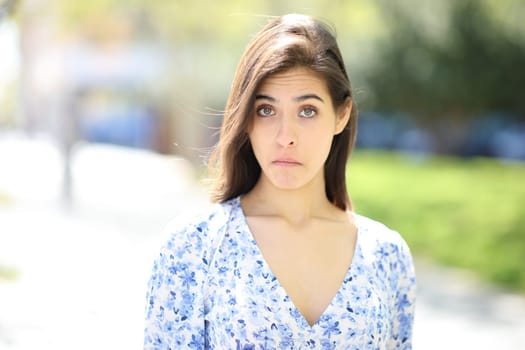 Front view portrait of a perplexed woman looking at camera in the street