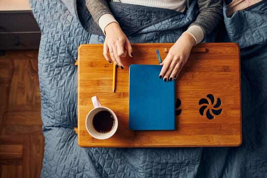 Young woman opening diary, writing journal. Making notes in diary sitting in bed at home