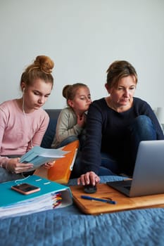 Women mother and daughter working learning remotely doing job homework during video chat call stream online course webinar lessons on laptop from home during COVID-19 quarantine. Women sitting on bed in front of computer looking at screen in company little girl playing around