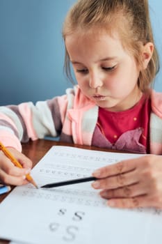 Little girl preschooler learning to write letters with help of her tutor. Kid writing letters doing a school work. Concept of early education