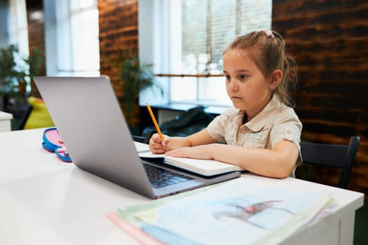 Engaged absorbed student doing her homework using laptop in after school club at primary school. Back to school. Child using technology on elementary computer science class. Smart little girl learning from educational application at school. Child solving riddles and puzzles on personal computer