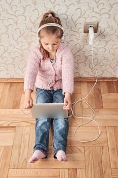 Little girl preschooler learning online solving puzzles playing educational games listetning to music and sounds using tablet and headpphones at home during pandemic quarantine