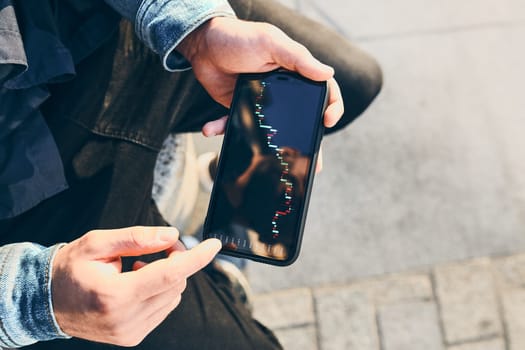 Person investing trading on stock cryptocurrency market using investing application on smartphone. Stock market investment in hand. Trader holding mobile phone looking at candle chart