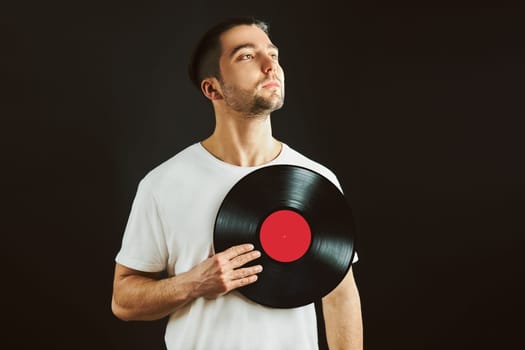 Man holding vinyl record over heart. Music passion. Vintage music style. Male holding old vinyl disk standing on black background. Retro music. Tribute to music