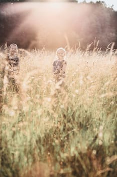 Little happy smiling kids playing in a tall grass in the countryside. Candid people, real moments, authentic situations
