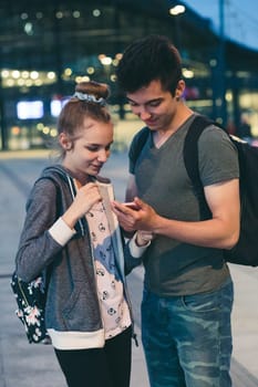 Young woman and man looking at screen of smartphone during walk in the city at night