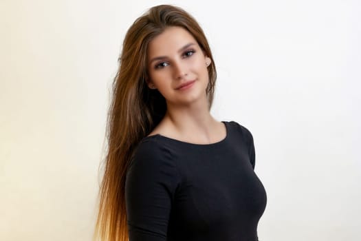 Attractive girl with long hair is posing smiling at the camera on the light background. Horizontally.