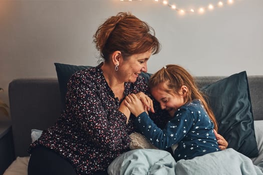 Mother playing with her little daughter in bed, having fun before going sleep. Mom tickling her cute daughter before bedtime