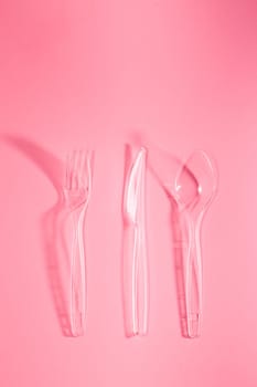 Plastic forks and knives scattered over pink background. Collecting plastic waste to recycling. Concept of plastic pollution and too many plastic waste. Copy space at the top