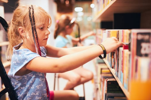 Schoolgirls looking for books in school library. Students choosing books. Elementary education. Doing homework. Learning from books. Back to school