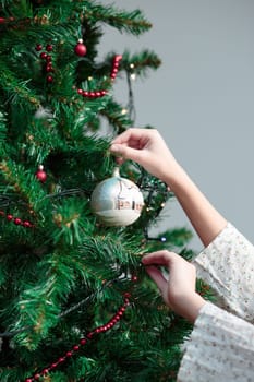 Young girl decorating Christmas tree with hand painted ball at home