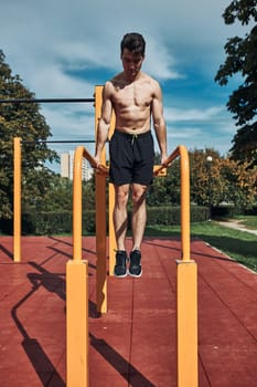 Young shirtless bodybuilder doing dips on parallel bars during his workout in a modern calisthenics street workout park