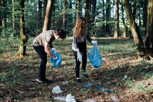 Young man and woman cleaning up a forest. Volunteers picking plastic waste to bags. Concept of plastic pollution and too many plastic waste. Environmental issue. Environmental damage. Responsibility for environment. Real people, authentic situations