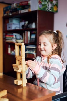 Little girl preschooler playing with wooden blocks toy building a tower. Concept of building a house