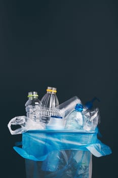 Heap of plastic bottles, cups, bags collected to recycling in a metal bin. Concept of plastic pollution and too many plastic waste. Trash with used plastic packagings over dark blue background with copy space at the top