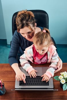 Little girl preschooler learning online solving puzzles playing educational games typing letters listetning to music and sounds with help of her mother using laptop computer and sitting at desk at home